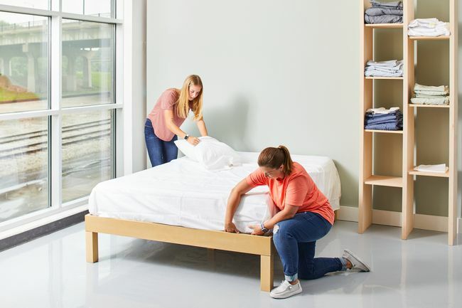 divas sievietes klāj gultu ar baltiem palagiem